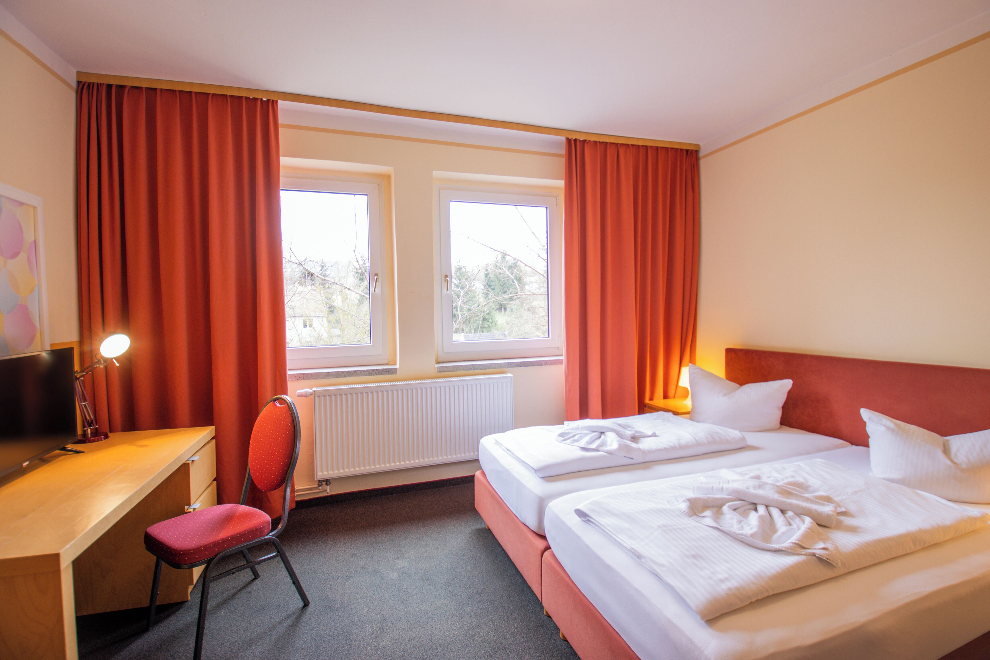 A hotel room with two beds, a desk, a chair, and a window with curtains.