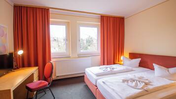A hotel room with two beds, a desk, a chair, and a window with curtains.