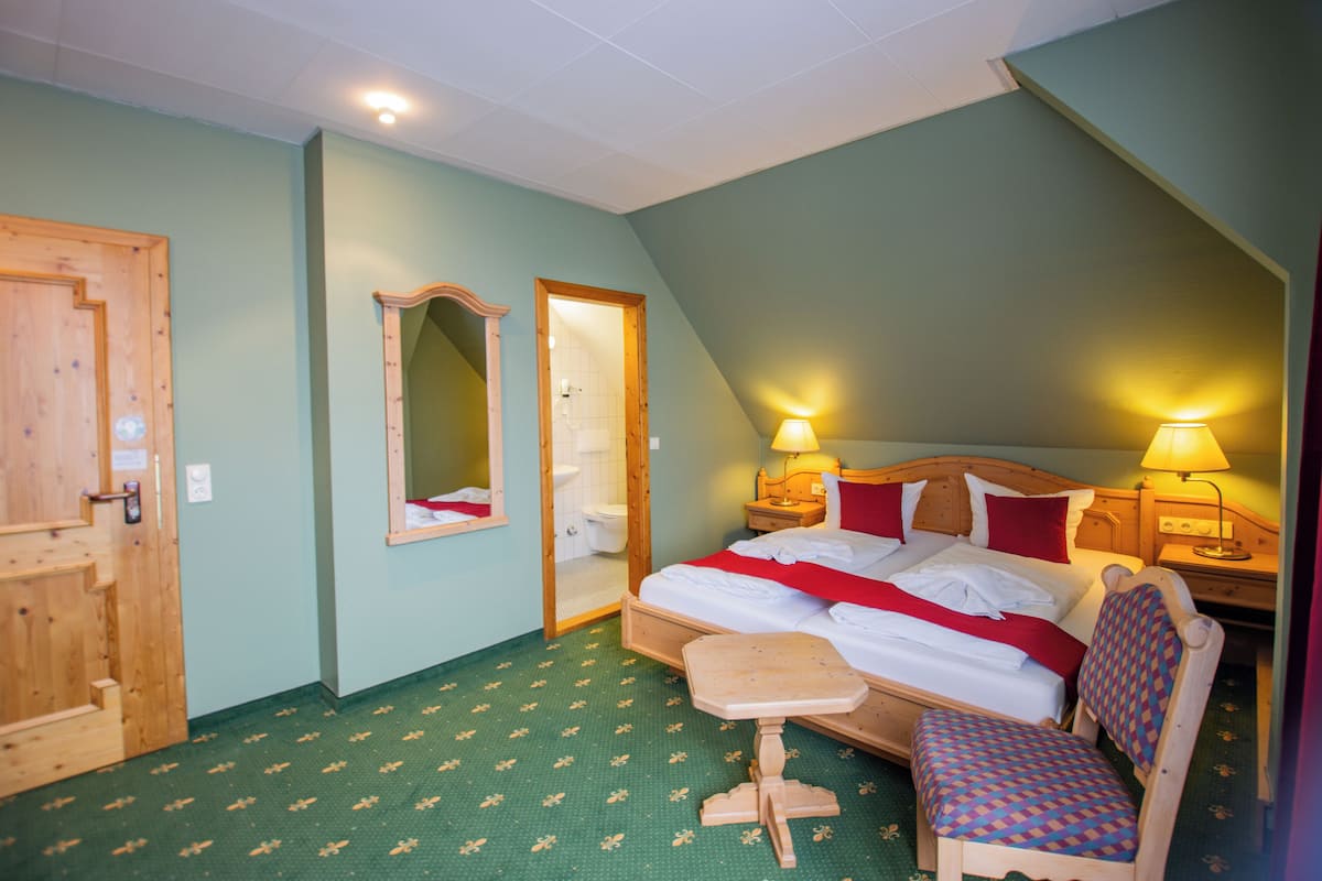 Ein Schlafzimmer mit Bett, Nachttischen, einem Spiegel, einer Holztür und einem kleinen Holzschemel.