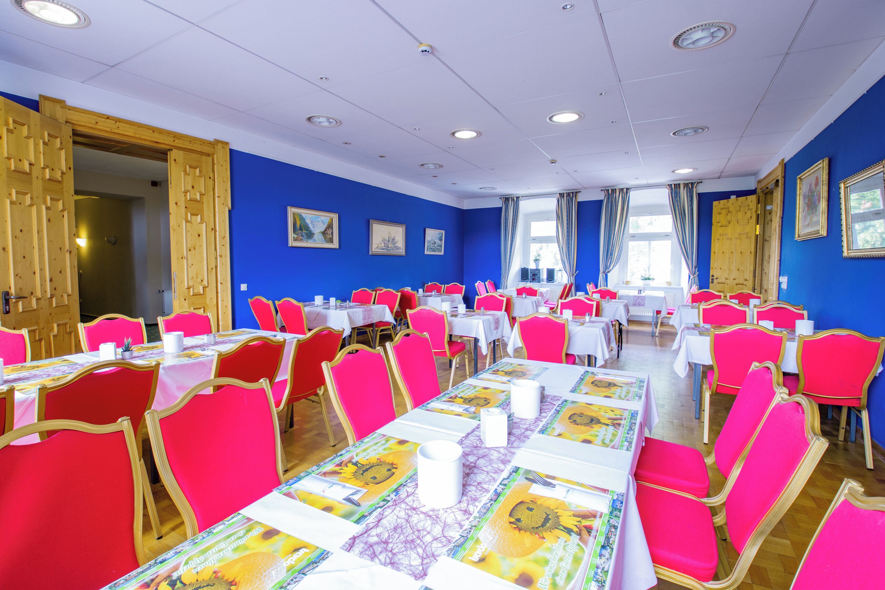 A dining area with tables set for multiple people, featuring bright red chairs and white tablecloths.