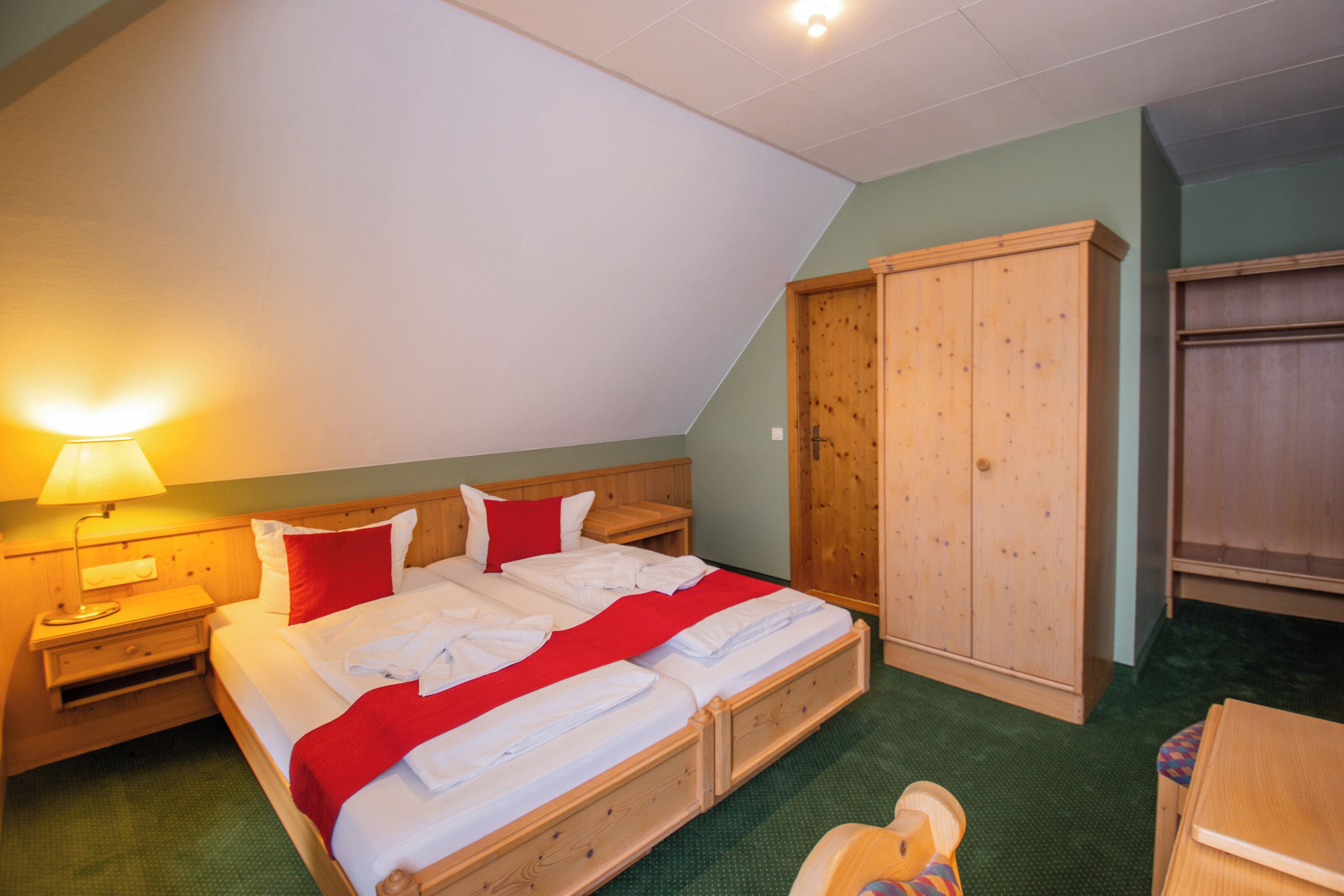 Un dormitorio con cama, armario de madera y mesita de noche con lámpara.