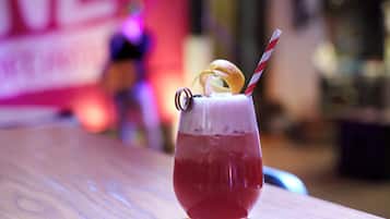 Ein Cocktail mit Zitronenscheibe und gestreiftem Strohhalm in einem Glas auf einem Holztisch.