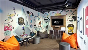 A modern lounge area with a dartboard, bean bags, and a television screen displaying 'aloft'.