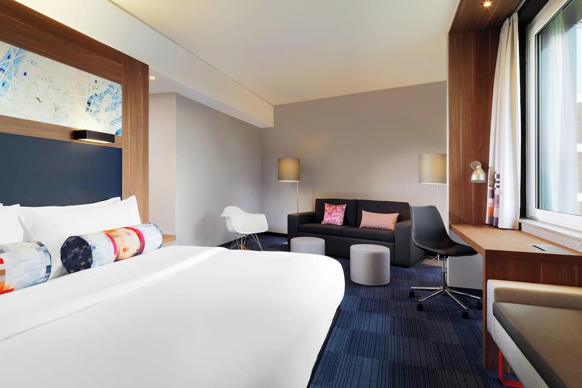 A modern hotel room with a large bed, a desk, a chair, and a sofa.