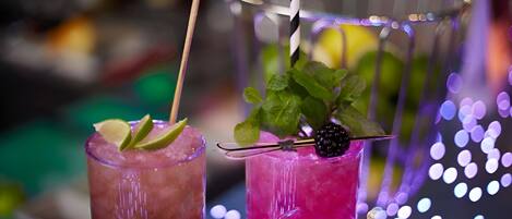 Two glasses of pink cocktails with lime and mint garnishes, one with a straw and one with a blackberry.