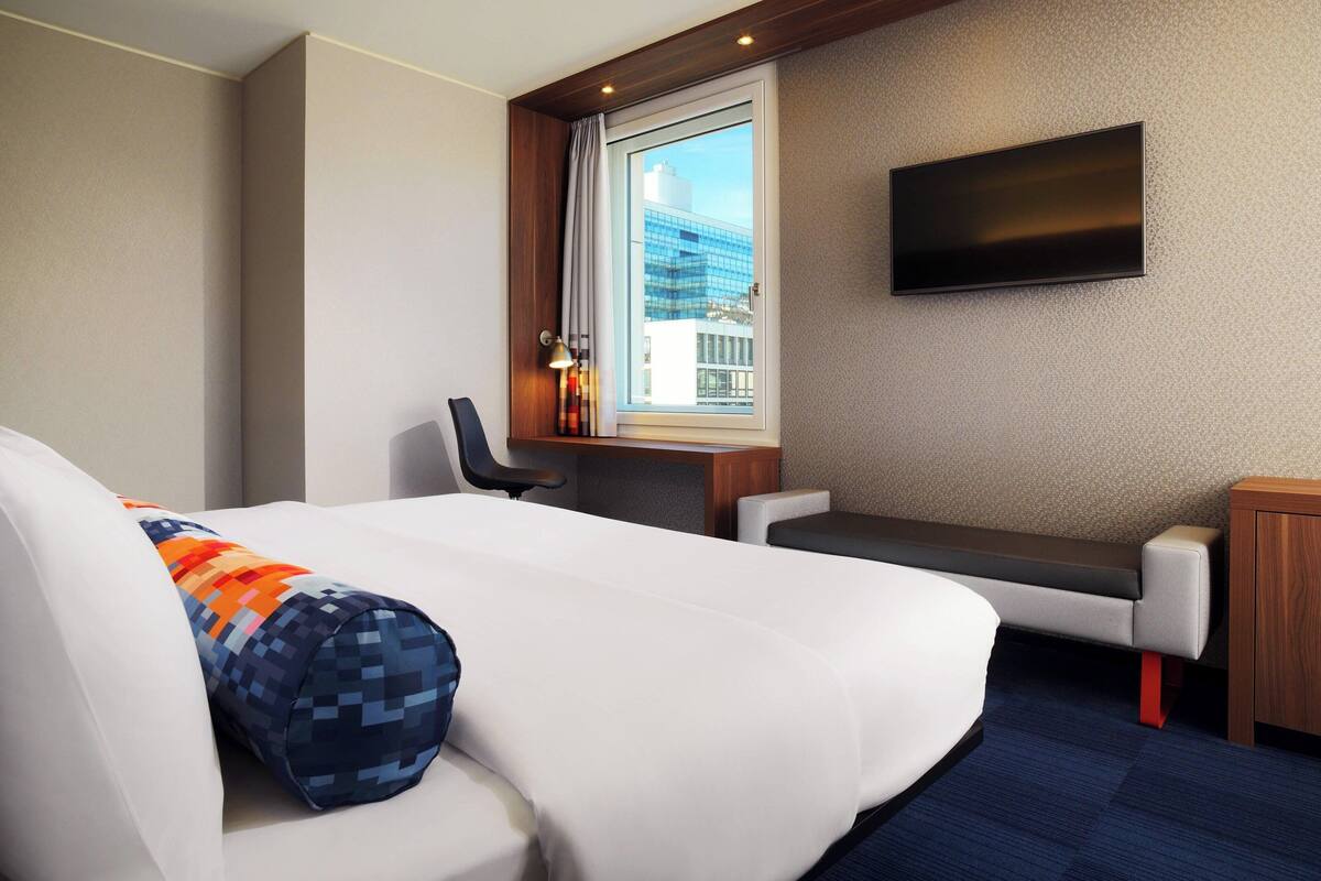 A hotel room with a bed, a desk, a chair, a TV, and a window with a city view.