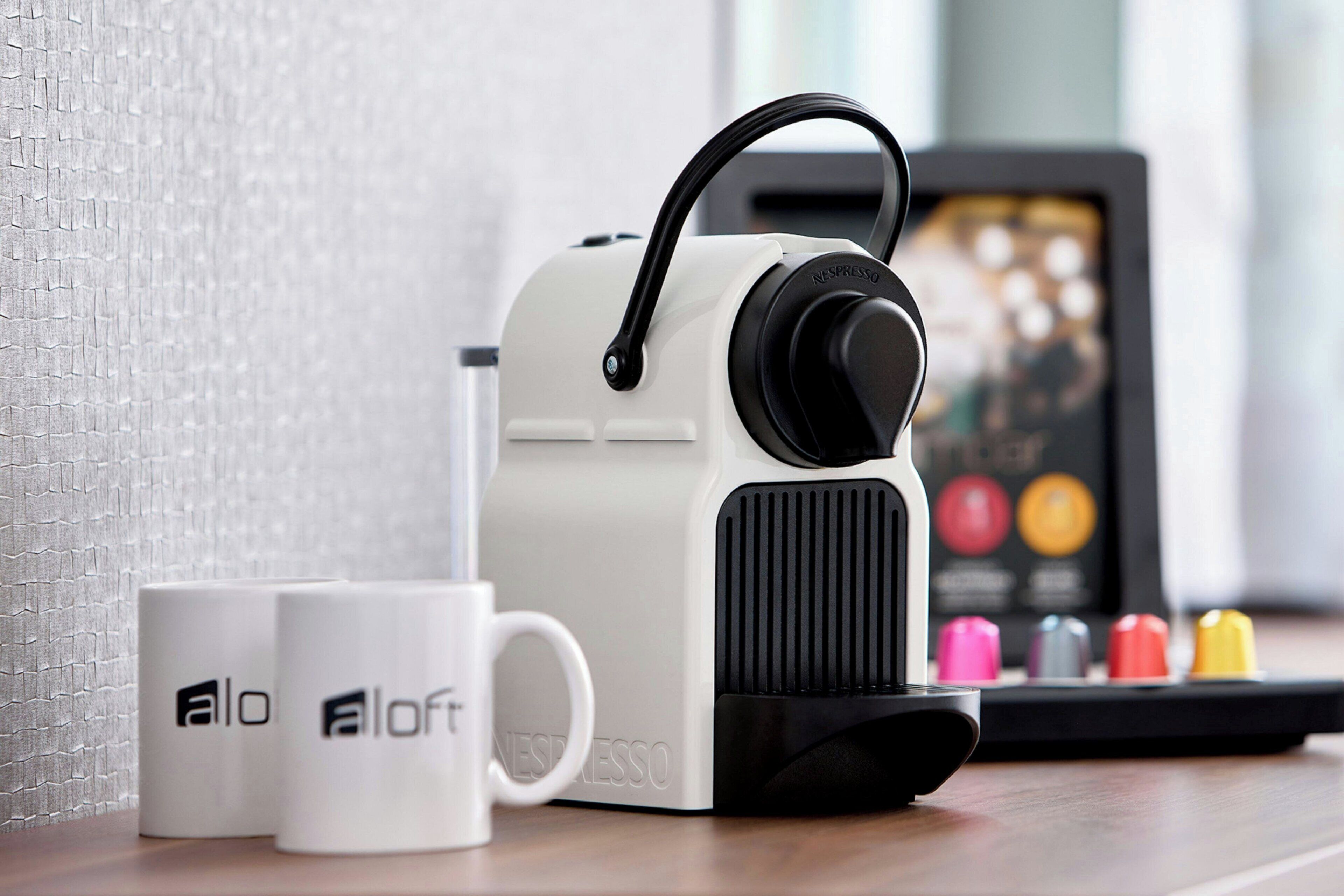 A coffee machine with a handle, two white cups with 'a loft' branding, and a coffee pod display.
