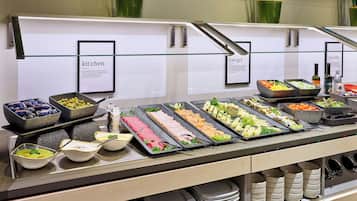 A buffet with various food options, including meats, cheeses, and vegetables, arranged on a glass counter with labels for each section.