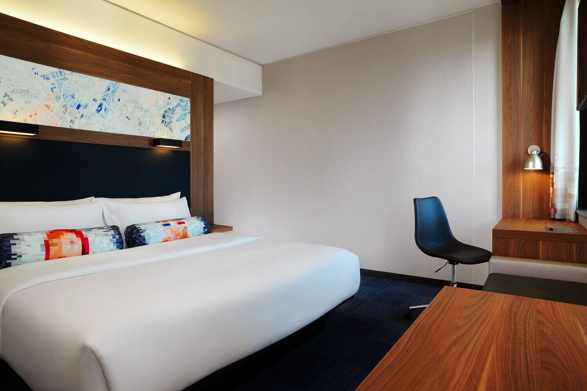 A hotel room with a large bed, a desk, a chair, and a map on the wall.