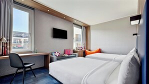 A hotel room with a bed, a desk, a chair, a TV, and a window.