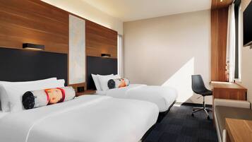 Habitación de hotel con dos camas, un escritorio, una silla y un ventanal grande.