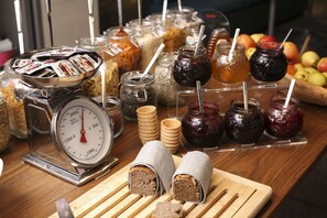 A buffet table with various food items, including jars of jam, a scale, and wrapped sandwiches. - Aloft by Marriott Munich (Munich)