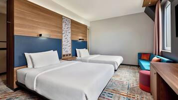 A hotel room with two beds, a sofa, a desk, and a patterned carpet.