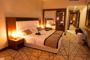 A hotel room with a large bed, a nightstand with a lamp, a mirror, and a patterned floor. - Mariana Hotel Erbil (Erbil)