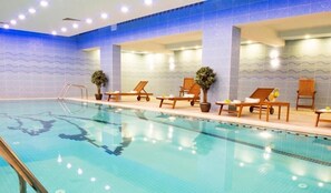 An indoor swimming pool with clear blue water, surrounded by wooden lounge chairs and potted plants. - Mariana Hotel Erbil (Erbil)