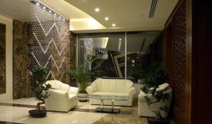 A modern lobby with a glass coffee table, two white sofas, and potted plants. - Mariana Hotel Erbil (Erbil)