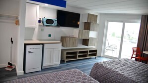 A hotel room with a bed, a small refrigerator, a microwave, a TV, and a sliding glass door to the outside.