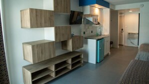 A compact living space with built-in wooden storage units, a kitchenette, and a television mounted on the wall.