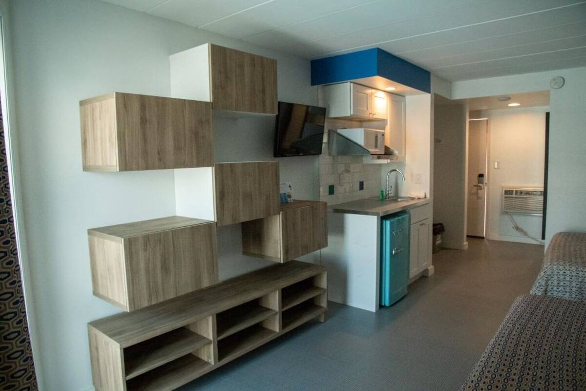 A compact living space with built-in wooden storage units, a kitchenette, and a television mounted on the wall.