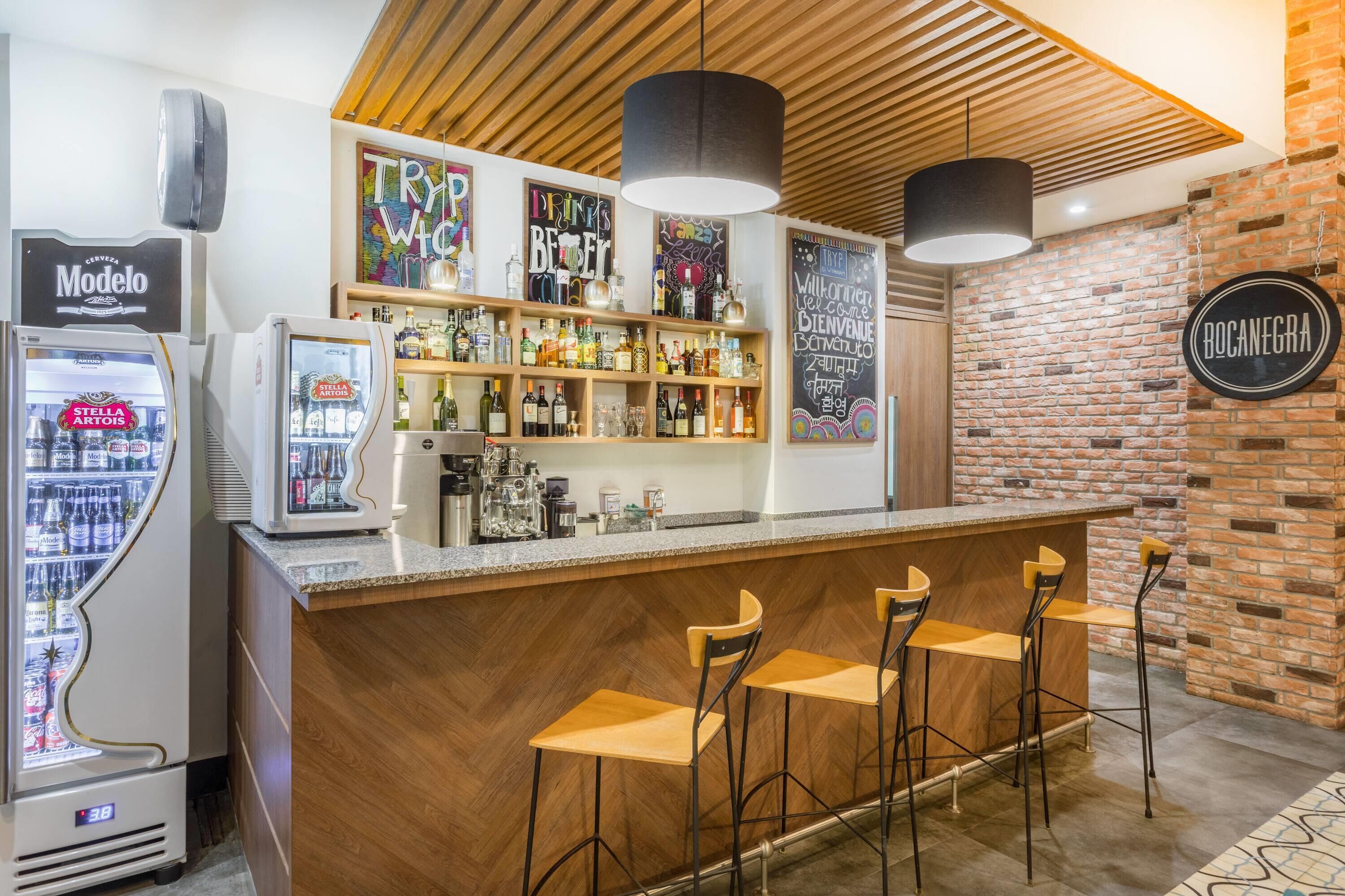 Zona de bar con mostrador de madera, taburetes y un refrigerador con el logo de Modelo.