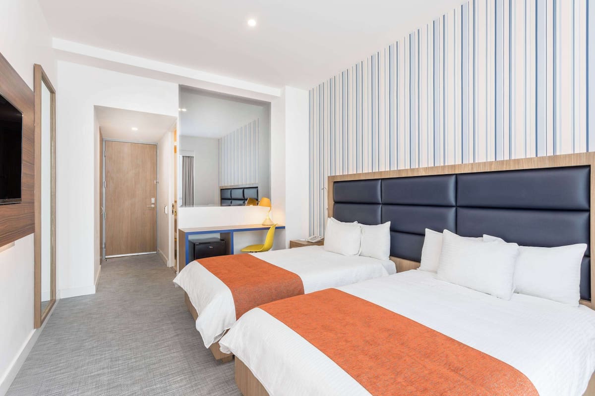 Ein Hotelzimmer mit zwei Betten, einem Schreibtisch, einem Spiegel und einem Fernseher.