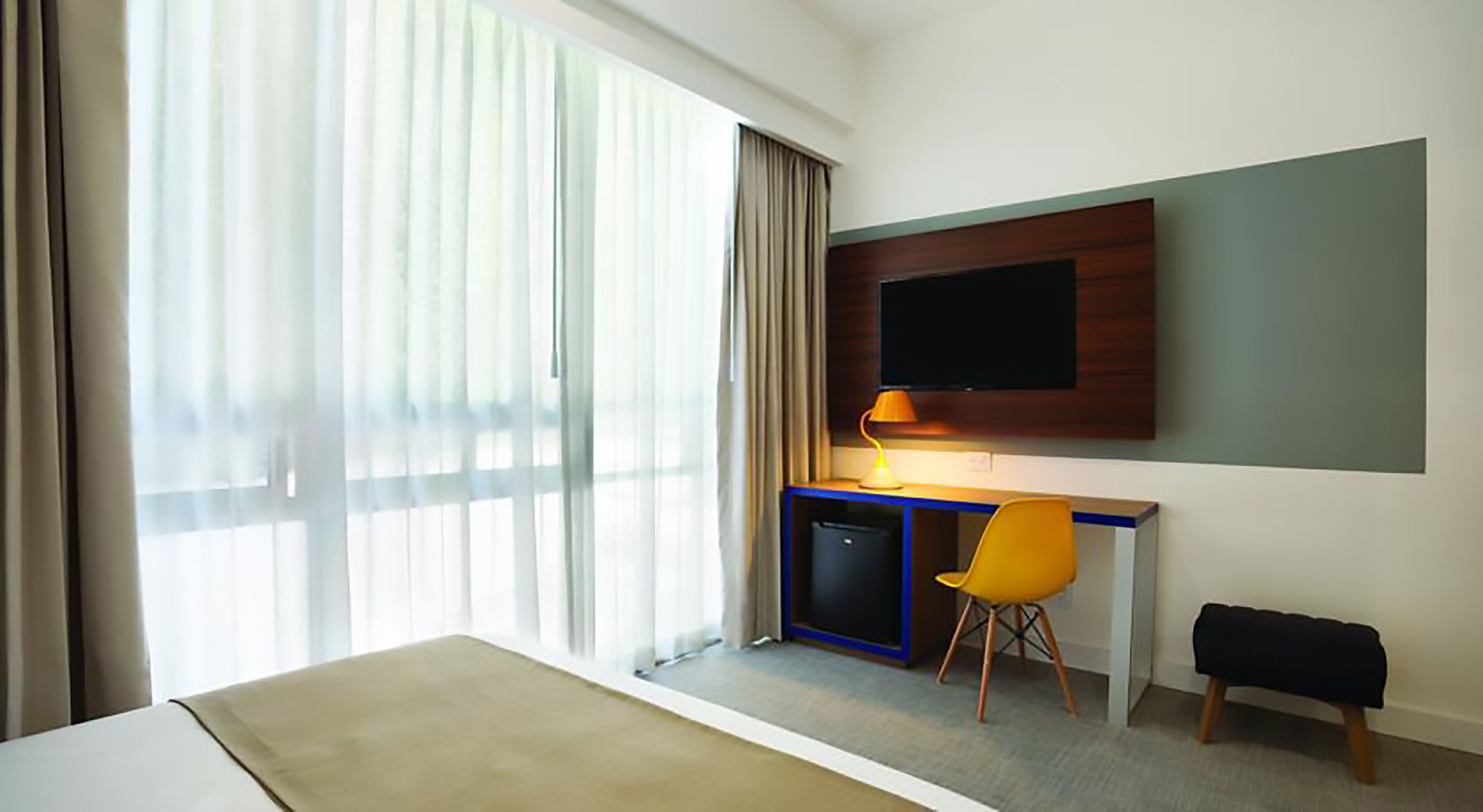 Habitación de hotel con cama, escritorio con silla, televisor y ventana con cortinas.
