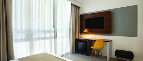 Habitación de hotel con cama, escritorio con silla, televisor y ventana con cortinas.