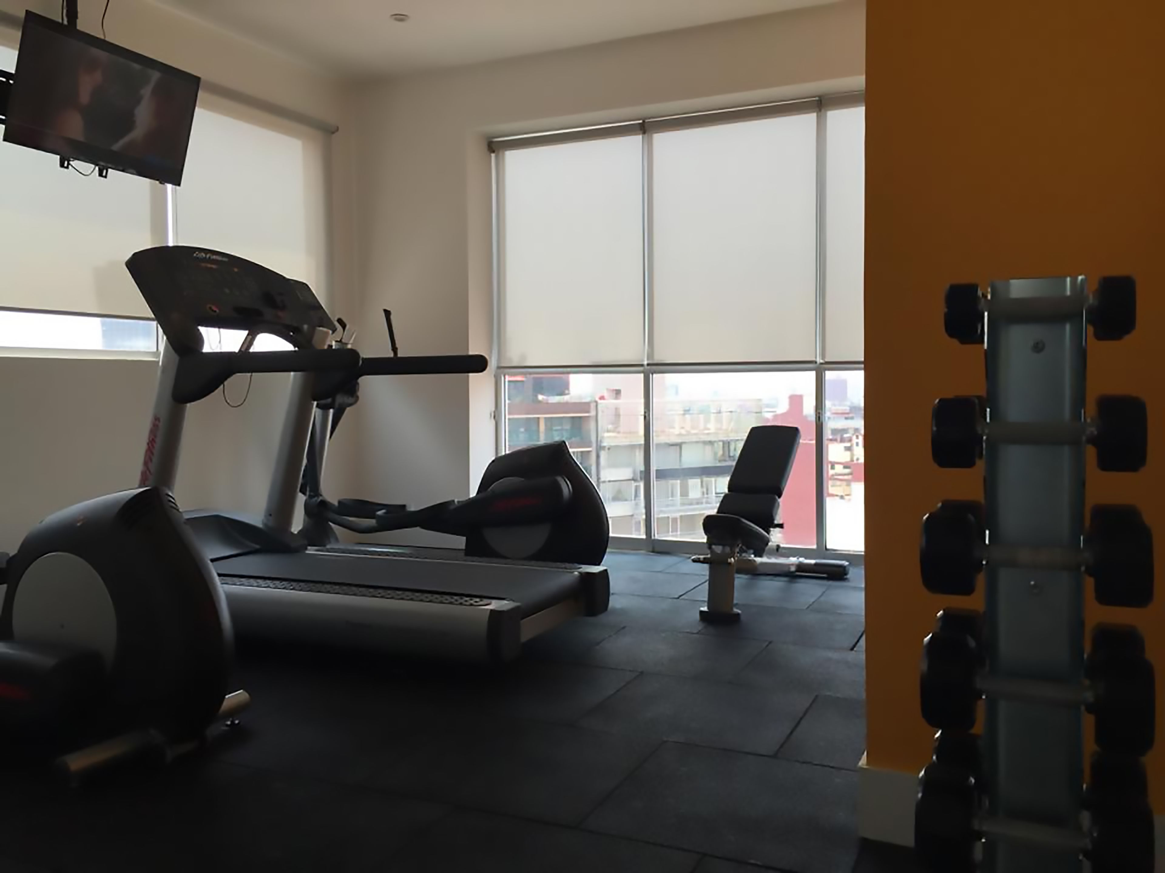 Un gimnasio con cinta de correr, pesas y una silla.