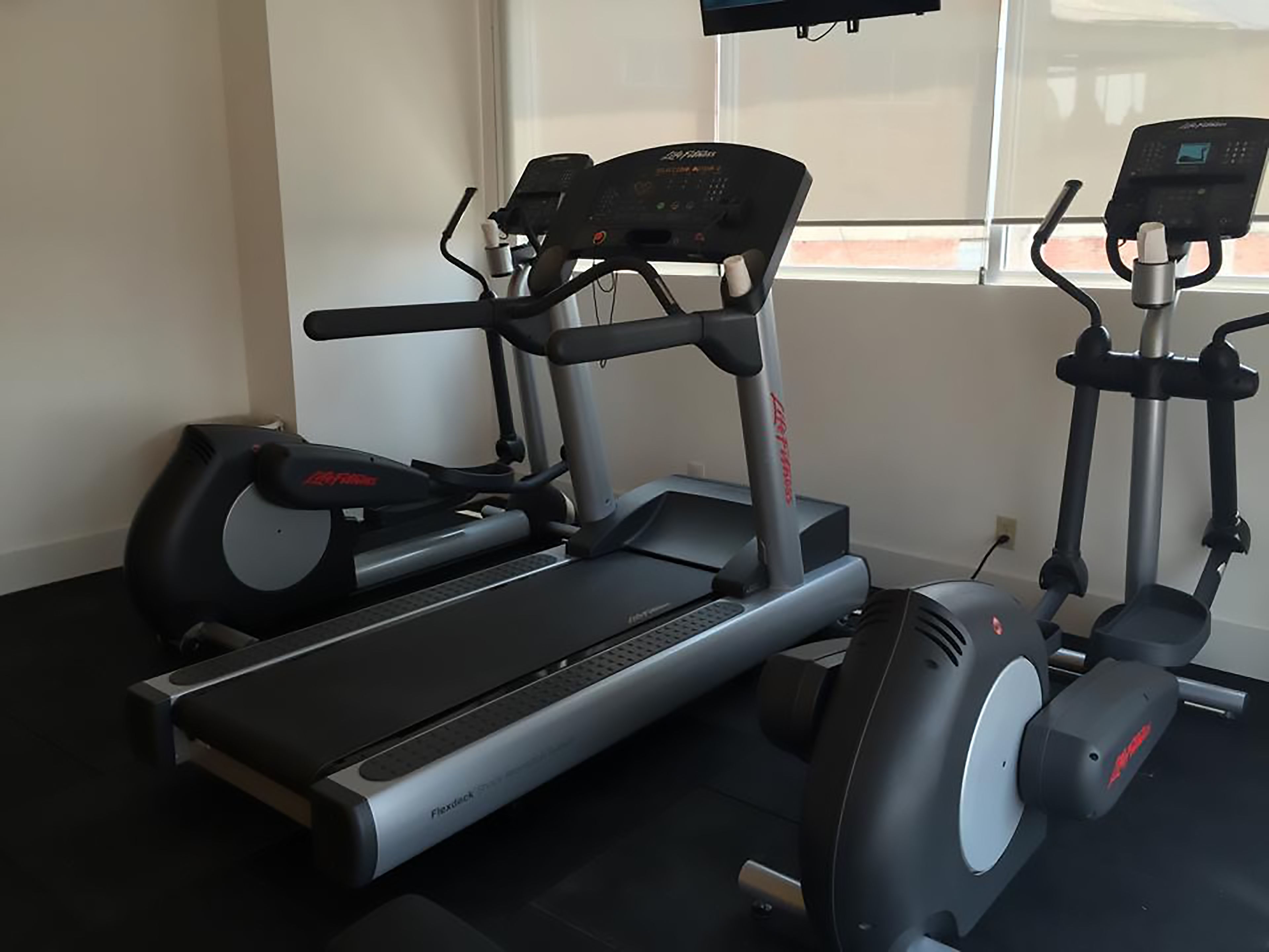 Uma academia em casa com esteira, elíptico e bicicleta ergométrica.