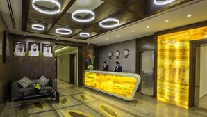 A reception area with a modern design, featuring a reception desk, a sofa with patterned cushions, and a wall with framed portraits. - Al Sarab Hotel (Dubai)