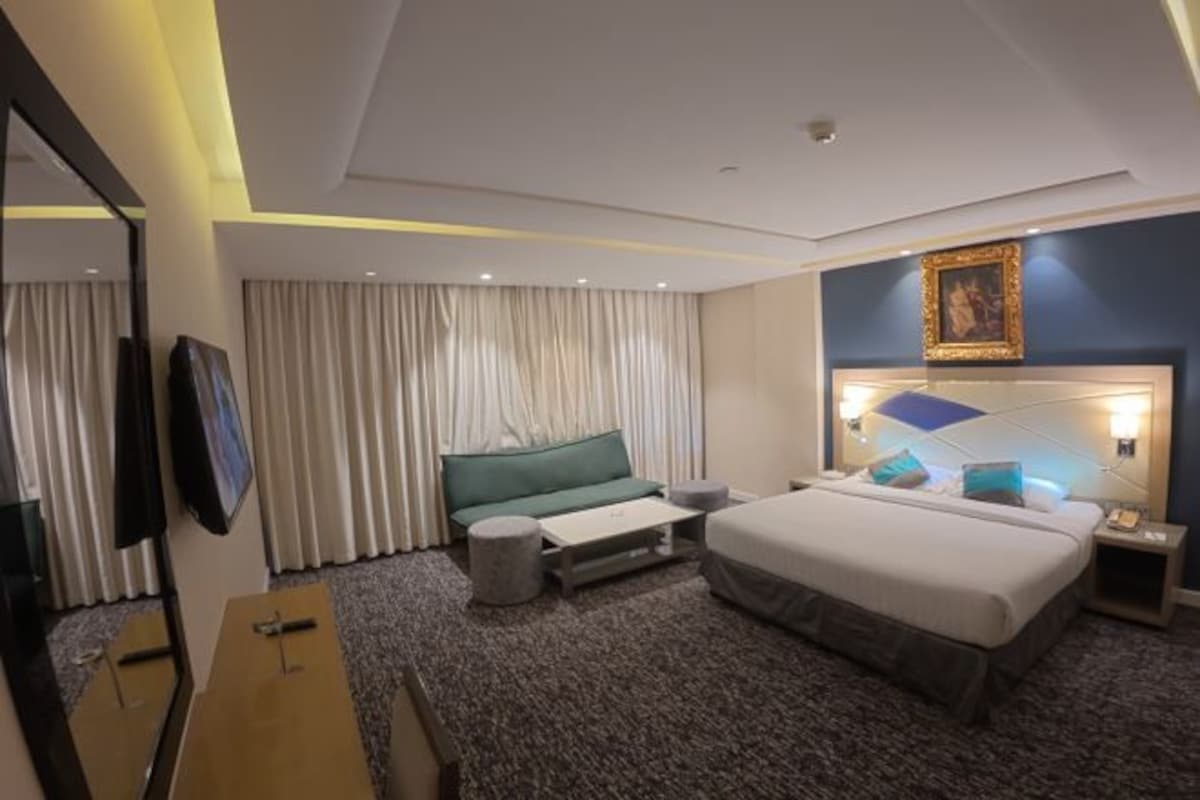 A hotel room with a bed, a desk, a chair, a TV, and a window with curtains.