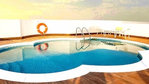 A swimming pool with a wooden deck, a lifebuoy, and a chair by the pool. - Al Sarab Hotel (Dubai)