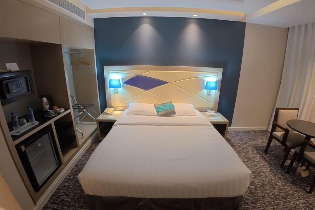 Una habitación de hotel con cama, mesitas de noche, escritorio, silla, un armario pequeño y televisor montado en la pared.