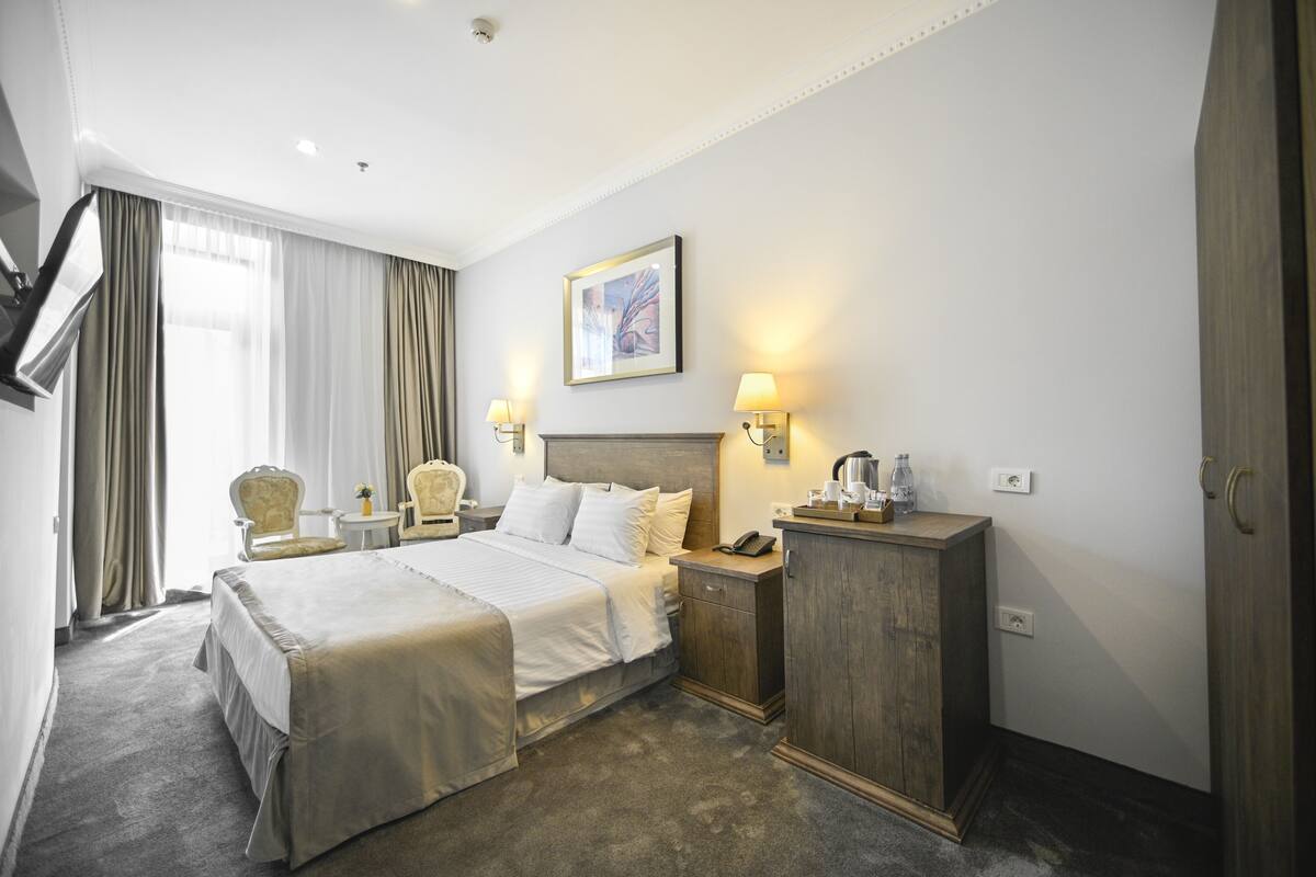 Ein Hotelzimmer mit einem großen Bett, einem Nachttisch, einem Holzkasten und einem Schreibtisch mit einer Lampe.