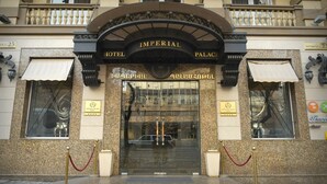 De ingang van het Imperial Hotel met een statig bogenpoort, dubbele deuren en een rode fluwelen touwbarrière.