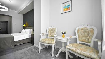A hotel room with a bed, two chairs, a small table, a vase with flowers, and a framed picture on the wall.