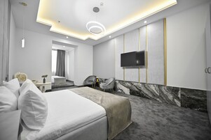 Een moderne hotelkamer met een groot bed, een zithoek, een flatscreen televisie aan de muur en een accentmuur van marmer.