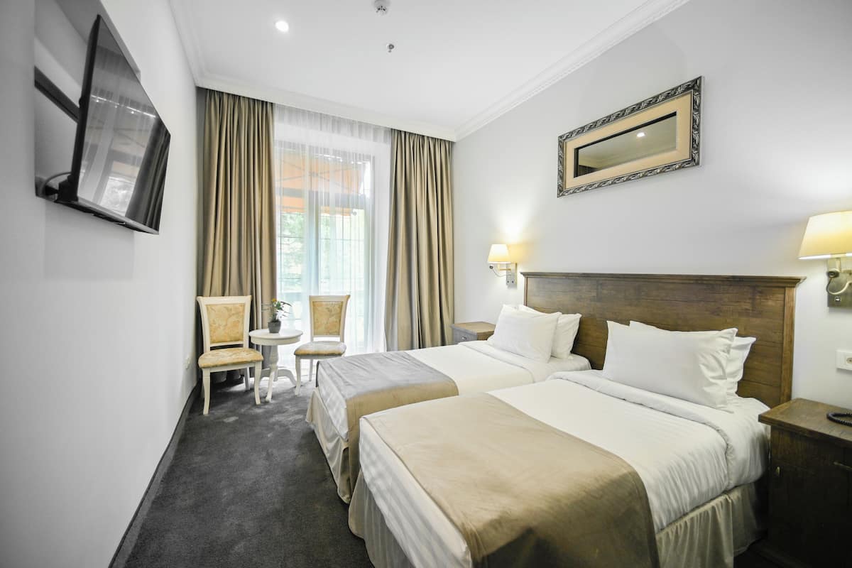 Ein Hotelzimmer mit zwei Betten, einem Fernseher, einem Sessel, einem kleinen Tisch und einem Fenster mit Vorhängen.