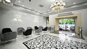 Een hotelhal met een patroon vloer, moderne stoelen, een kroonluchter en uitzicht op de straat.