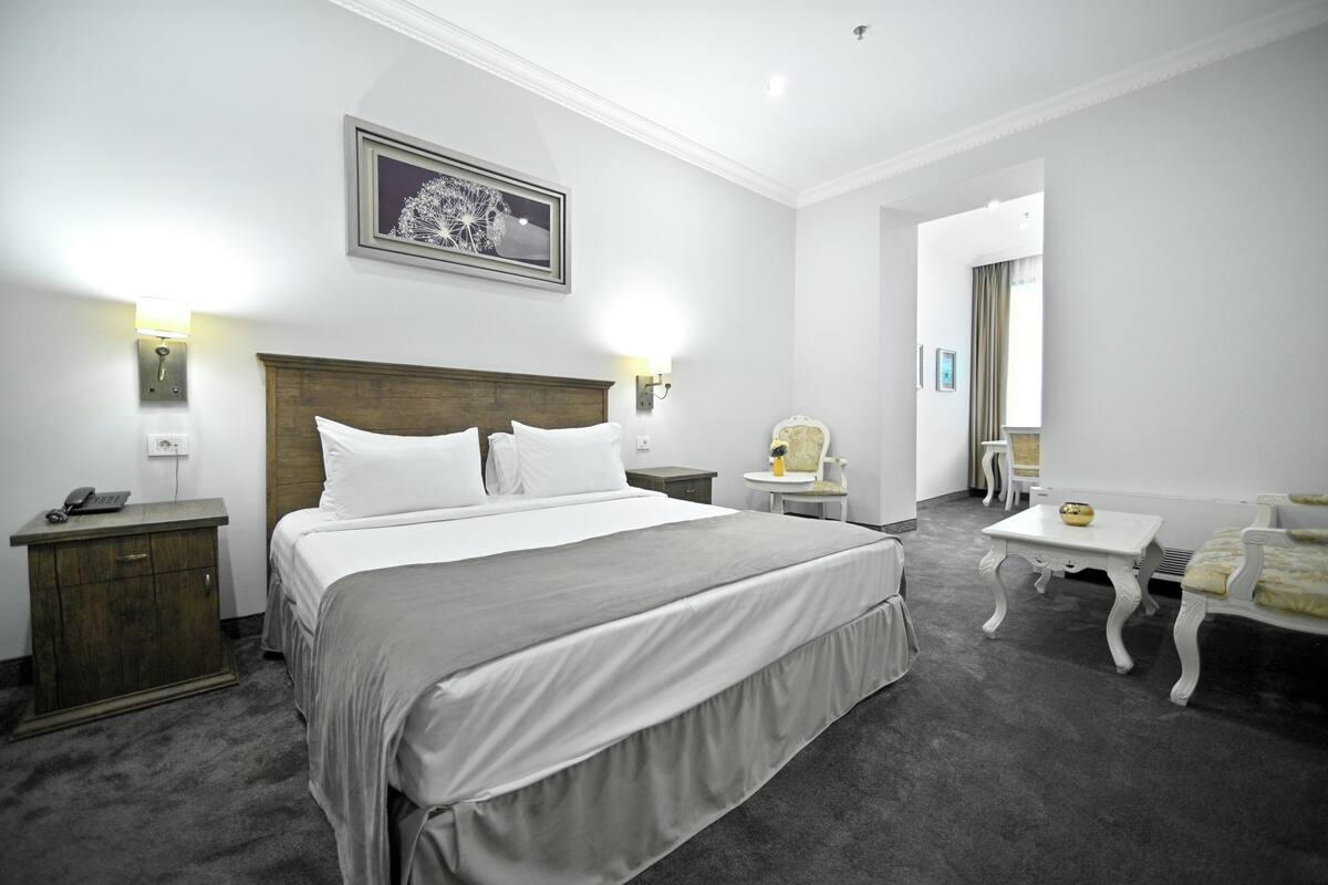 Ein Hotelzimmer mit einem großen Bett, Nachttischen, einem Sessel, einem kleinen Tisch und einem Spiegel.