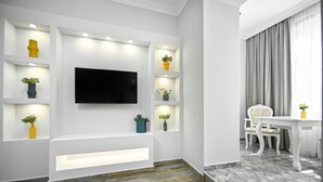 Een moderne woonkamer met een flatscreen televisie aan de muur, inbouwverlichting, een witte tv-meubel en een eethoek met een tafel en stoelen.