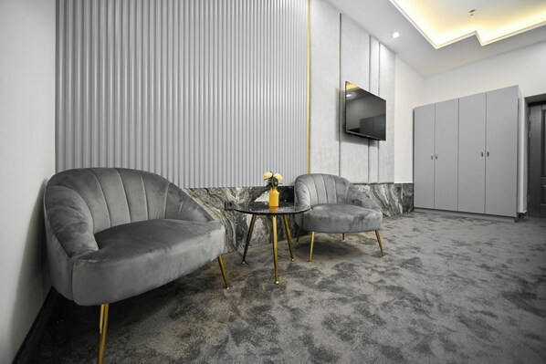 A modern room with two grey upholstered chairs, a small round table, and a TV mounted on the wall.