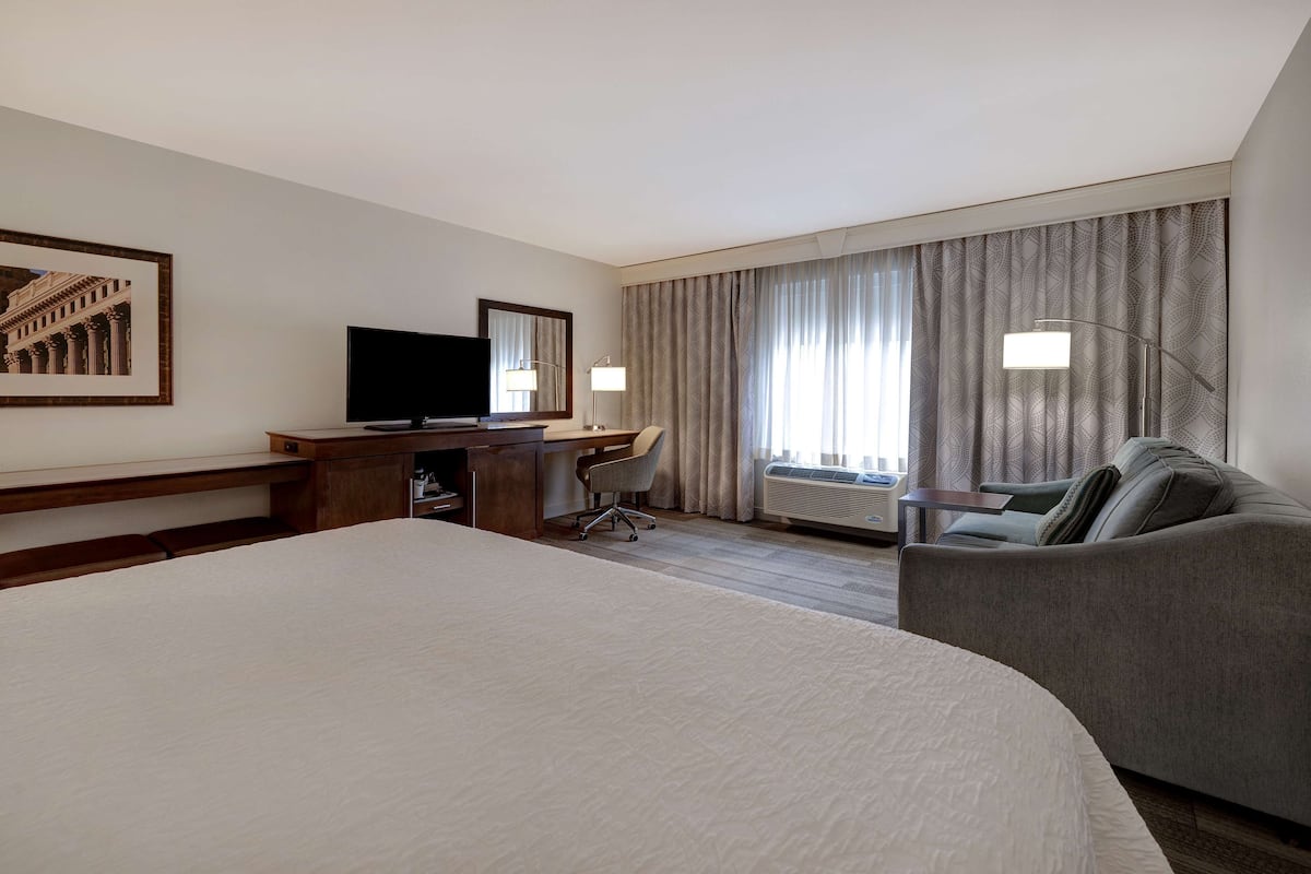 A hotel room with a large bed, a desk with a chair, a television, and a sofa.