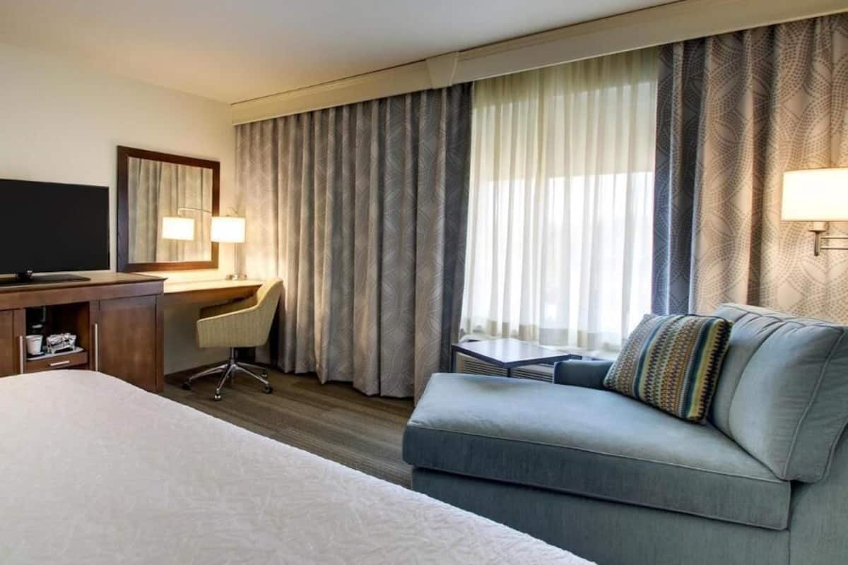 A hotel room with a bed, a desk, a chair, a sofa, a TV, and curtains.