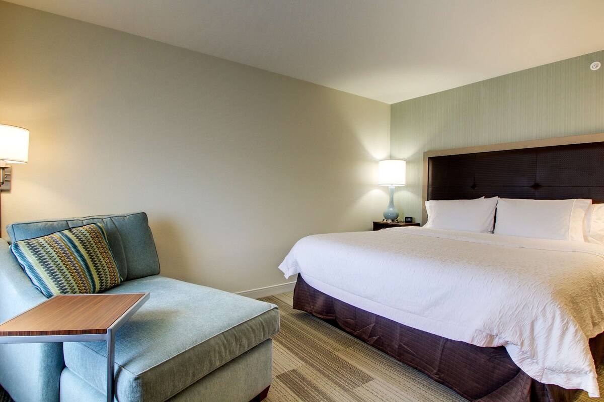 A hotel room with a bed, a sofa, a small table, and two bedside lamps.