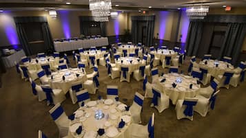 Un salón de banquetes con mesas redondas dispuestas para cenar, cada una con manteles blancos y fajas azules.