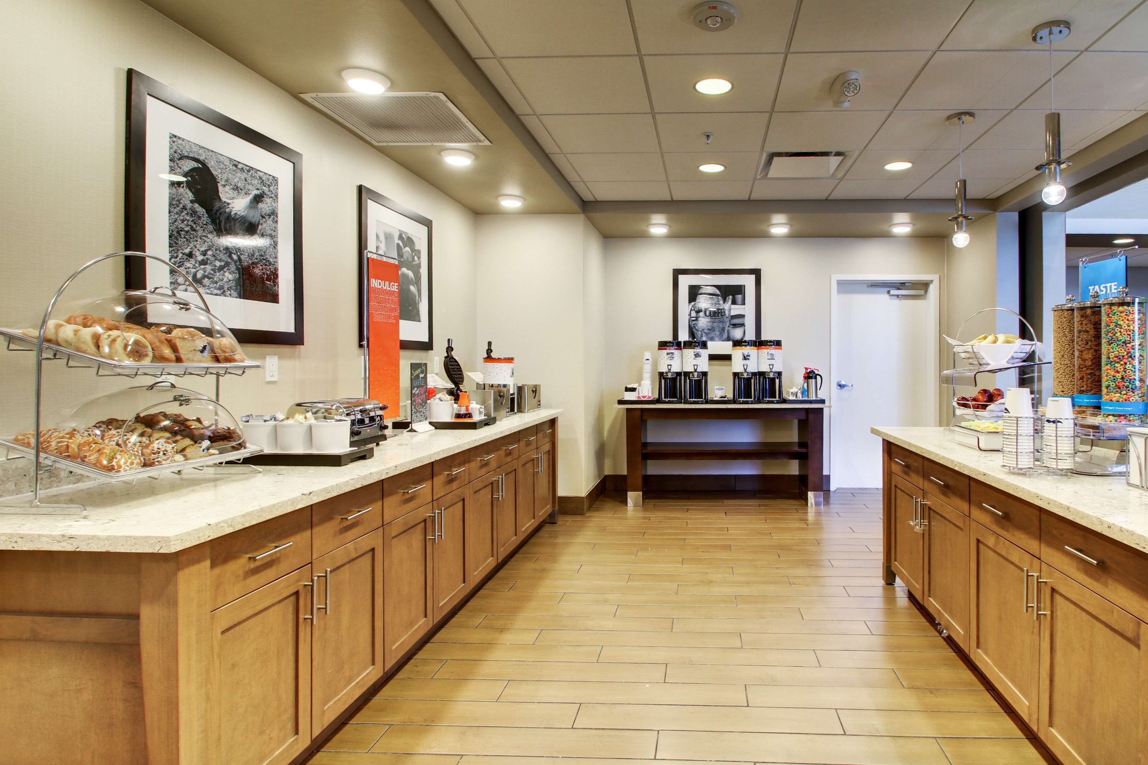 A hotel kitchen with wooden cabinets, a long countertop with food items, and a coffee station.