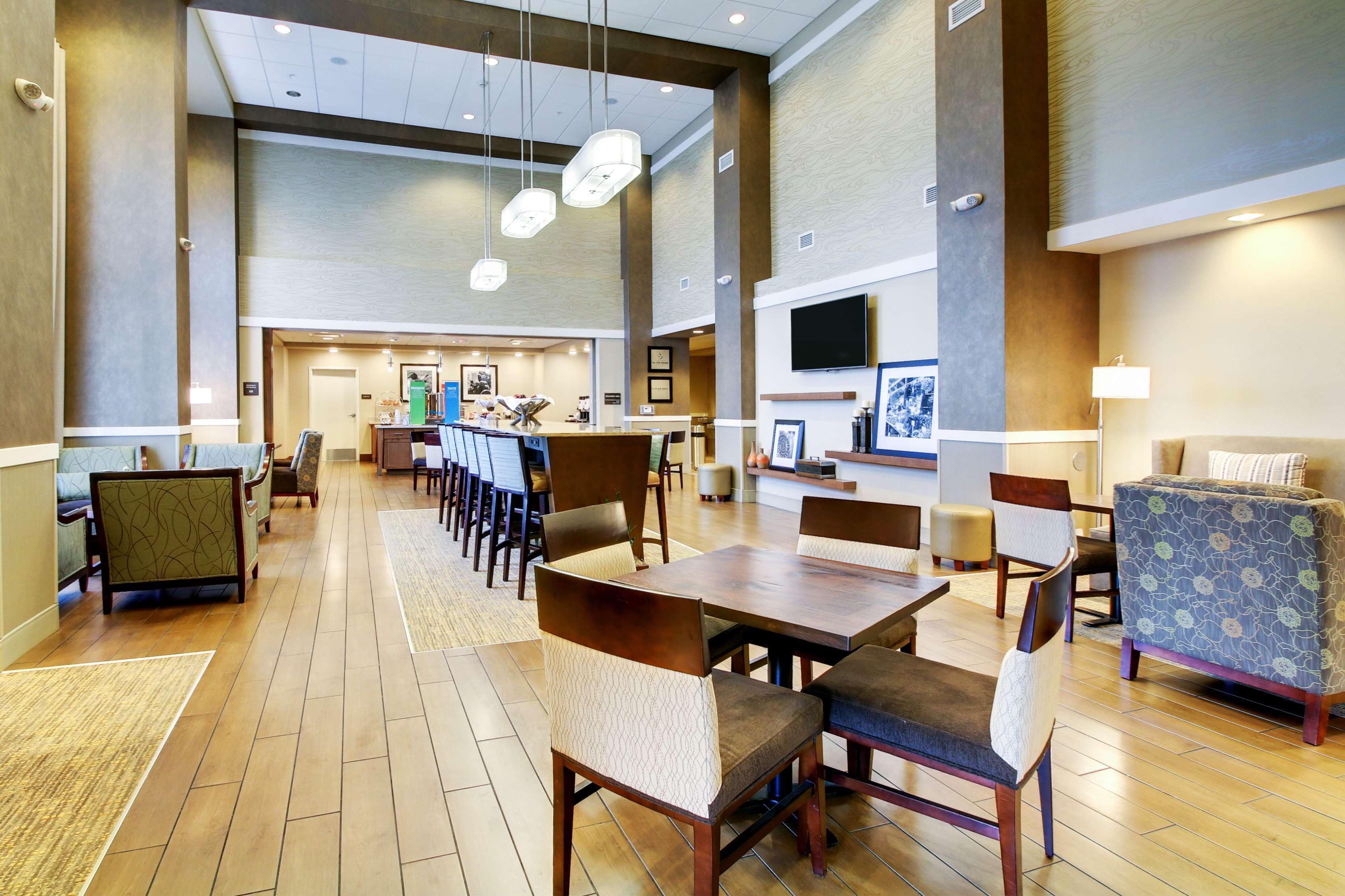 A spacious hotel lobby with a long reception desk, multiple seating areas, and a television mounted on the wall.