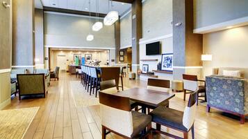 A spacious hotel lobby with a long reception desk, multiple seating areas, and a television mounted on the wall.