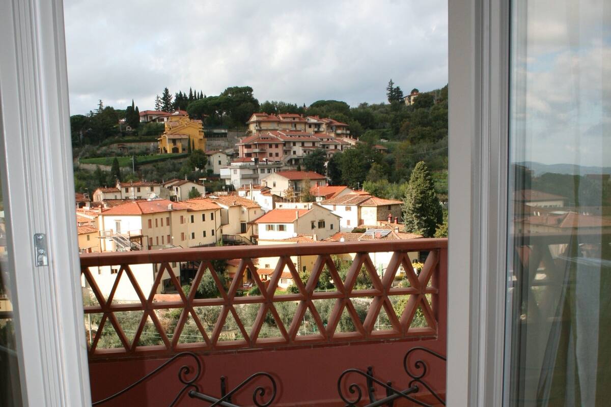 A balcony with a wrought iron railing overlooking a town with terracotta-roofed buildings.